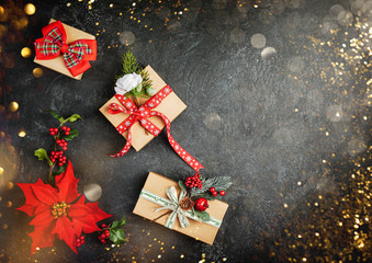 Christmas gifts, decorations and poinsettia flowers on black background. Creative winter holiday concept. Flat lay.