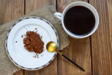 Brown vegetable carob (Ceratonia silica) in powder form without caffeine. Natural tasty drink made from carob. A cup with hot carob, a saucer with powder and a spoon on a wooden background.
