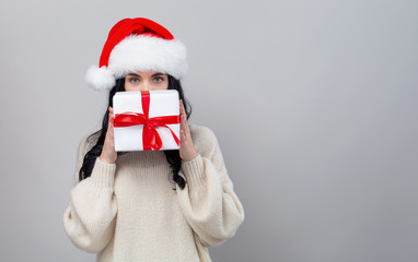 Young woman with santa hat holding a gift box on a gray background