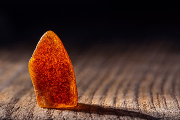 Natural amber. A piece of yellow transparent natural amber on large piece of dark stoned wood.