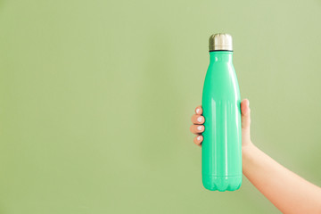 Female hand with sports water bottle on color background