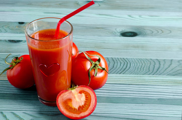 Tomato juice in a transparent bowl with a straw and a heart tomatoes on a wooden background concept