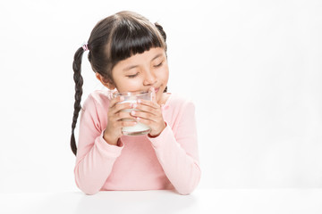 Cute little girl in casual dress in the hands holding glass of fresh milk looks happy,isolated on white background.