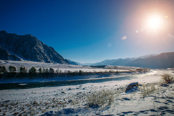 Stunning views of the ice-free Katun river among the snow-capped peaks. Valley in the mountains on a sunny winter day. Magnificent panorama of the Altai mountains.
