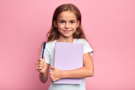 girl holding a book , pen. Back to school concept.isolated pink background, studio shot. lifestyle, free time, kid is ready to study.