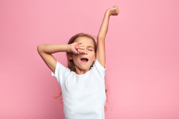 cute girl child with long blond hair yawns sweetly, stretching her arms, kid wants to sleep, isolated pink backround, tiredness. close up portrait - 298648663