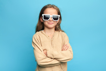 Little smiling happy model with sunglasses standing with crossed arms . Isolated over blue...