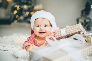Cutre little girl in Santa's hat lying among Christmas gifts.