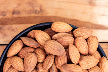 Close up raw peeled almonds seed in bowl on wooden background.