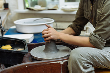 The girl sits at the Potter's wheel and creates a pot of ceramics. A Potter makes pottery out of clay behind a mechanical circle.