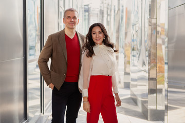 Fashion style Clothes, business casual. Respectable Businessman Wearing brown jacket and sweater and Woman in red pants and a stylish white shirt looking at camera and smiling