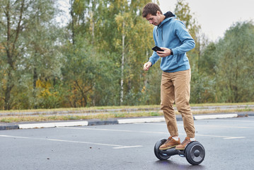 Obraz premium Man riding on the hoverboard and using smartphone outdoor