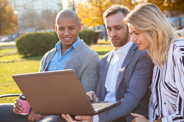 Mature business people browsing online together, using computer on their meeting outdoors in the park