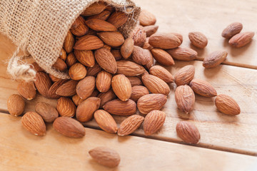 Close up raw peeled almonds seed in sack on wooden background..