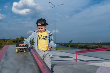 little boy 3-5 years old, summer on sports field in city, autumn on street, playing skateboard, practicing skateboarding, casual wear, a baseball cap and jeans. Weekend break.