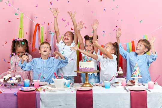 happy children enjoying confetti, close up photo, isolated pink background, studio shot