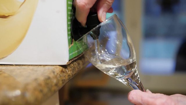 Woman pouring glass of white wine from wine box container.