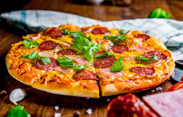Pepperoni Pizza with Mozzarella cheese, salami, ham, Spices and Fresh basil. Italian pizza on wooden table background