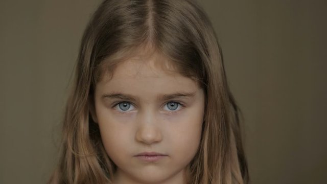 Portrait little young girl with blue eyes looking at camera. Young serious child looking at camera. Closeup. Indoors.  Sad little kid girl portrait looking.
