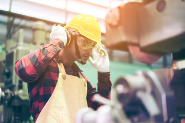 Manufacturer or Metal worker wearing safety glasses and protective helmets using lathe in order to machine or operating drilling machine concentrating on production plant job of production department