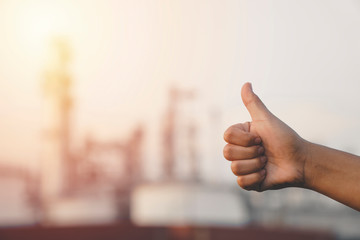 close up hand of worker or engineer woman showing thumbs up sign on Industrial view at oil refinery plant form industry zone with sunrise and cloudy sky background,blur with copy space