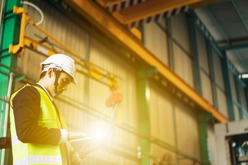 Engineer or worker with safety helmet holding Laptop using engineering software or control the CNC...