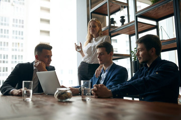 three office workers discussing a problem, while blonde woman standing behind them with a glass of water. modern office room