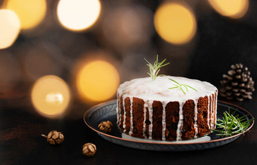 Traditional Christmas cake with fruits and nuts on a dark table and black background. Dessert for the winter holidays. Christmas decorations and lights. Copyspace. Bokeh