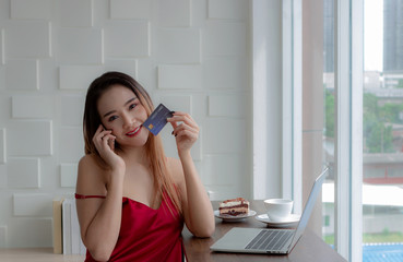 Beautiful businesswoman wearing a red dress for the holidays. Sit and relax in the living room. Talking on the phone credit card loans. Eating coffee and snacks on the table happily.
