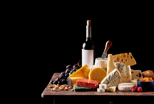 Various types of cheese and bottle of red wine on rustic wooden table