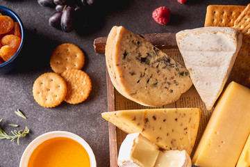 Various types of cheese in wooden box, honey, nuts, crackers, grapes