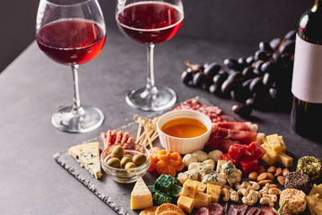 Red wine with different kinds of cheese, charcuterie assortment, crackers, grapes, nuts and berries