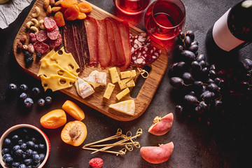 Red wine with different kinds of cheese, charcuterie assortment, crackers, grapes, nuts and berries