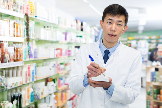 Chinese male is checking medicine with notebook in pharmacy