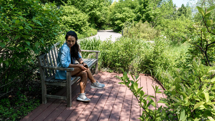 Asian woman sitting on bench on a brick patio surrounded by plants