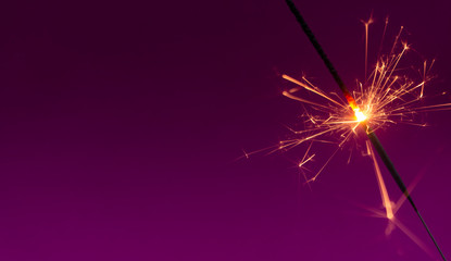 Obraz premium Burning christmas sparkler on purple background with room for text
