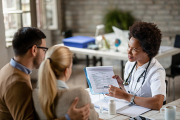 Black female doctor going through medical reports with a couple at clinic.