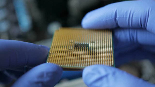 CPU in hands of a technician. The processor is being examined for apparent defects. In Modern Electronic Manufacturing Factory Design Engineer Holds Microchip  . Close-up a New Generation Microchip.