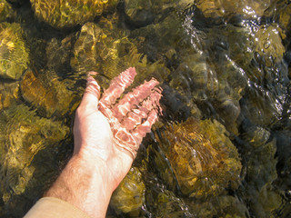 Touch river water with hand. Touch clear water with stone under, play inside water with hand, touch river with hand. Collect water with male hand