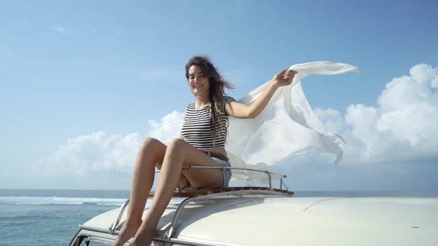 beauty woman enjoy blow wind with waving white scarf on the retro van roof at the beach