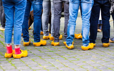 Close up of blue jeans legs of group of people wearing traditional wooden clogs during guided city...