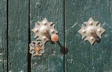Green wooden door with texture and metal hardware and star-shaped locks.