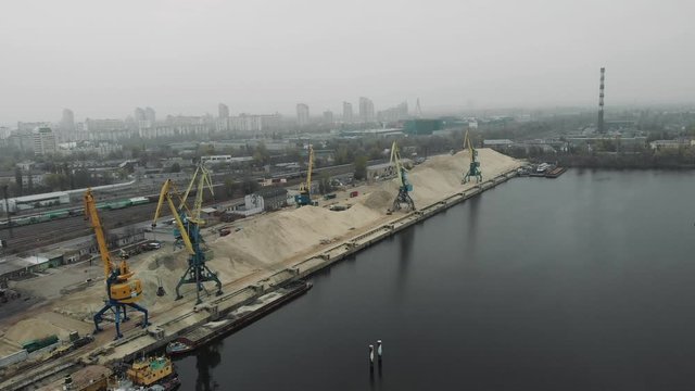 Port working cranes extracting sand from barge and scow in docks on river bank. Extraction of river sand in docks of industrial city