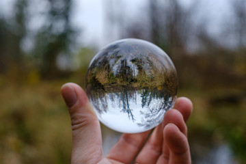 male hand holding crystal glass ball against nature background with reflections