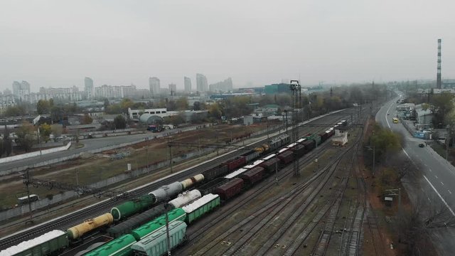 Aerial shot of industrial city and cargo freight train moving along the street with wagons filled with goods and fuel tanks