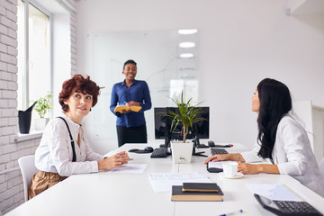 African business coach representing business plan to caucasian ladies in office, white interior