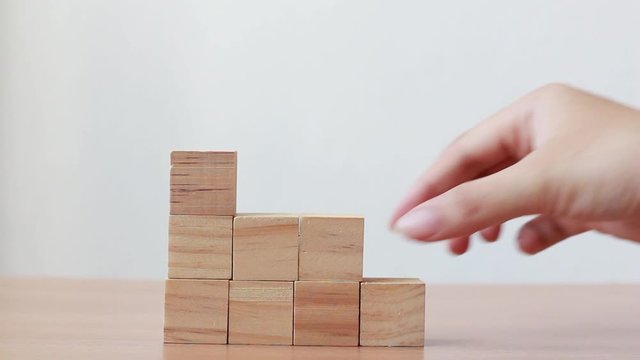 Hand putting wood cube on top of wood block stacking as step stair.business growth to success.