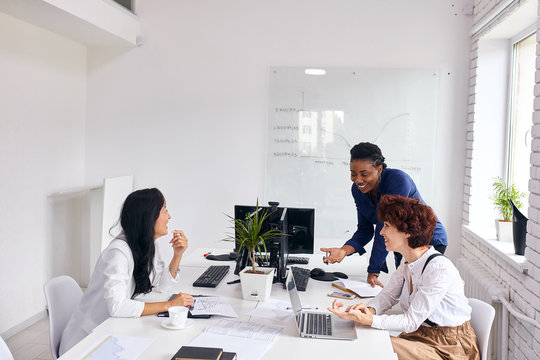 Positive african female coach smiling speak with caucasian representatives about business deal in office with white interior