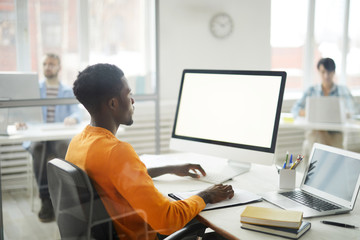Side view portrait of young African-American man using computer in office, focus on blank white...
