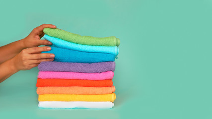 Close-up of hands putting stack of fresh bath towels. stack of multi-colored clean towels on a blue...